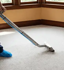 Steam carpet cleaning technician using a hot-water extraction wand on a residential carpet, wearing blue protective shoe covers Honolulu, HI.