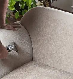 Professional upholstery cleaner deep-cleaning a fabric sofa with a handheld extraction tool and hose Honolulu, HI.