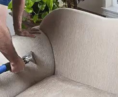 Professional upholstery cleaner deep-cleaning a fabric sofa with a handheld extraction tool and hose in Honolulu, HI.